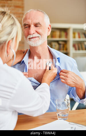 Femme médecin examine senior man avec le stéthoscope lors d'une visite à domicile Banque D'Images