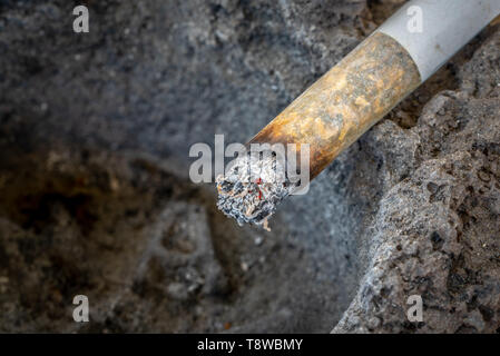 Un mégot de cigarette avec des cendres sur le bord d'un cendrier fait de lave solidifiée. Close up. Copier l'espace. Banque D'Images