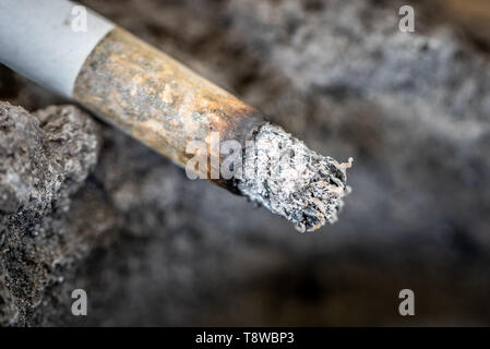 Un mégot de cigarette avec des cendres sur le bord d'un cendrier fait de lave solidifiée. Close up. Banque D'Images