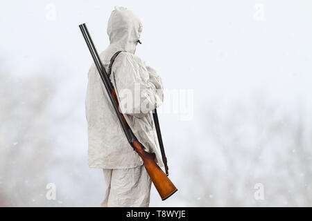 Hunter en blanc camouflage avec un fusil sur son épaule dans le champ d'hiver Banque D'Images