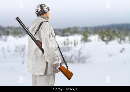 Hunter en blanc camouflage avec un fusil sur son épaule dans le terrain de chasse en hiver Banque D'Images