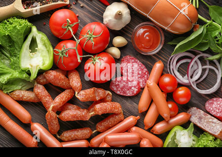 Différents types de saucisses avec la sauce et les légumes sur fond de bois Banque D'Images