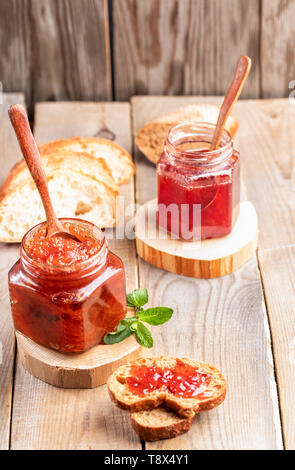 Deux pots de verre de fraise fait maison et confiture de pommes avec des cuillères en bois et les tranches de pain sur la vieille table en bois rustique. Dainty faite maison. Banque D'Images