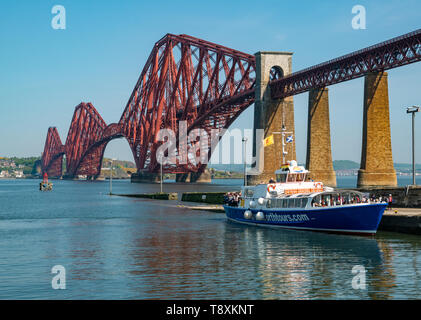 South Queensferry, Ecosse, Royaume-Uni, 15 mai 2019. Météo France : une chaude journée ensoleillée sur le Firth of Forth côte à l'emblématique Forth Rail Bridge et un bateau de tourisme chargement de passagers Banque D'Images