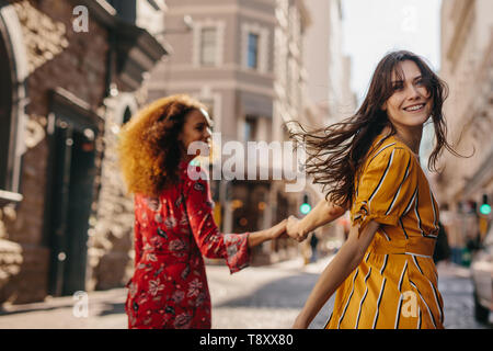 Vue arrière de deux jeunes femmes marchant ensemble sur la ville se tenant la main. Femme regardant par-dessus son épaule alors qu'il marchait avec son amie à l'extérieur. Banque D'Images