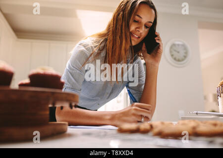 Chef pâtissier de l'ordre d'écriture féminine et de parler sur smartphone. La prise de commandes par téléphone confiseur en cuisine. Banque D'Images