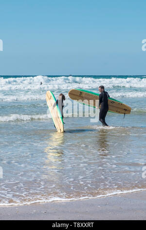 Les surfeurs à pied dans la mer à l'hotspot surf dans Fistral Newquay en Cornouailles. Banque D'Images