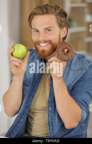 Jeune-homme avec barbe est le choix d'Apple ou beignet sucre gras Banque D'Images