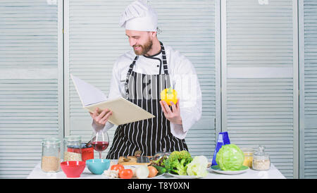 Selon recette. Chef barbu homme à la cuisson des aliments. Guy lire livre de recettes. Concept d'arts culinaires. Apprendre l'homme recette. Améliorer les compétences de cuisson. Guide de cuisson ultime pour les débutants. Livre des recettes de famille. Banque D'Images