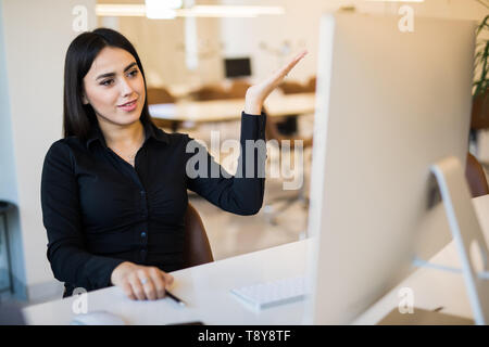 Jolie jeune femme avec des mains en face de l'écran pc sitting in office Banque D'Images