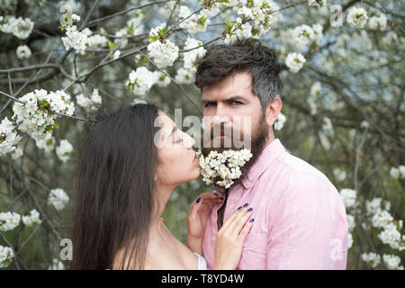 Couple amoureux au jardin fleuri. Tendre femme aux longs cheveux noirs et bel homme avec de minuscules fleurs blanches en barbe. L'homme brutal embrassant son Banque D'Images