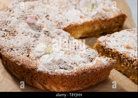 Gâteau aux pommes maison saupoudrée de sucre glace et décoré de fleurs de pommier sur papier parchemin brun, cut Close-up, selective focus. Banque D'Images