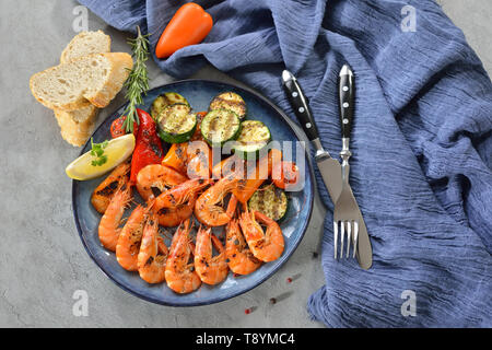 Gambas grillées avec des légumes méditerranéens servis sur une plaque bleue sur une table avec regard concret Banque D'Images