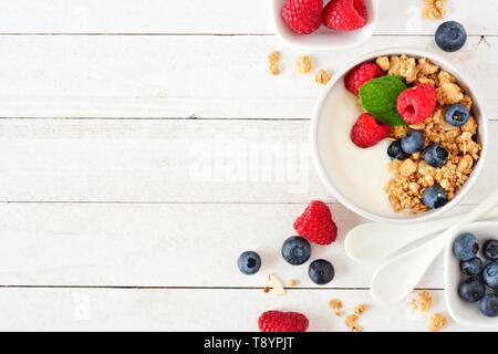 Le yogourt saine avec des framboises, bleuets et granola. Voir ci-dessus, sur une frontière côté fond de bois blanc. Copier l'espace. Banque D'Images