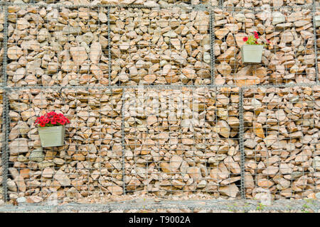 Mur de clôture gabions de treillis d'acier avec des pierres décorées de fleurs. Banque D'Images