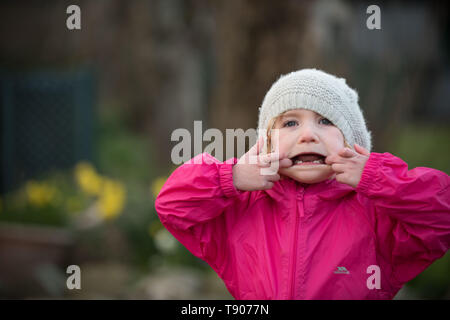 Petite fille dans hat pulling faces in garden Banque D'Images