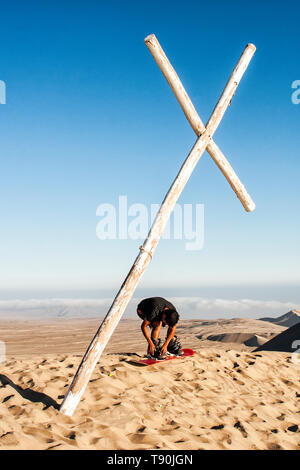 Sandboarder sous une croix sur le sommet du Cerro Toro Mata. Acari, Département d'Arequipa, Pérou. Banque D'Images