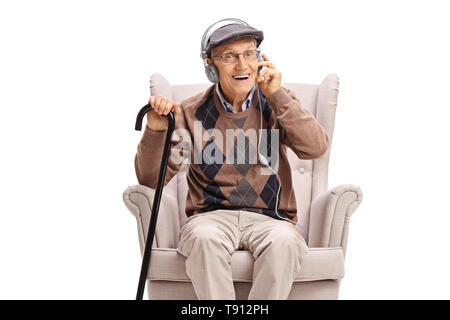 Un homme âgé assis dans un fauteuil et écouter de la musique sur écouteurs isolé sur fond blanc Banque D'Images