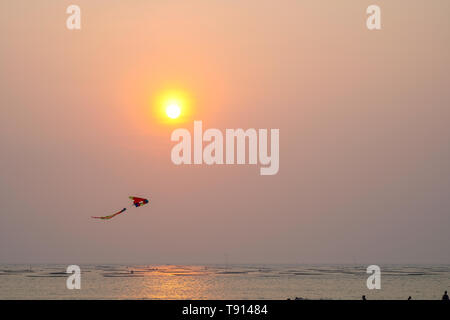 Vue de la plage avec un coucher de soleil rougeoyant jaune dans l'horizon avec un cerf-volant. Banque D'Images