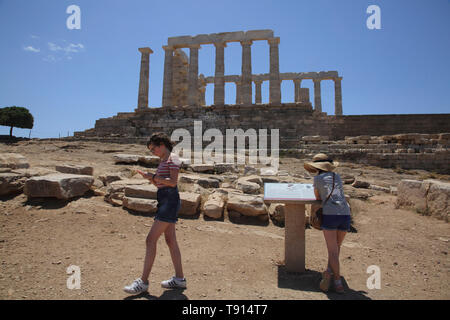 Attica Grèce Cap Sounion Temple de Poséidon les Soeurs l'un à la recherche d'informations sur le bord de l'autre à son téléphone portable Banque D'Images