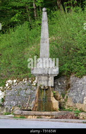 Fontaine en pierre vieille de plusieurs siècles en forme d'obélisque avec de l'eau douce partiellement couvert de mousse humide entouré avec des dalles en pierre Banque D'Images