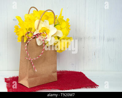 Bouquet de jonquilles jaune générique en sac de papier sur toile en bois blanc et rouge Banque D'Images