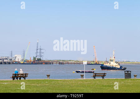 Gravesend, Kent. UK. Un couple de personnes âgées assis sur un banc à Gravesend, Promenade à la recherche de bateaux et un remorqueur sur la Tamise. Banque D'Images