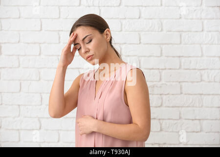 Femme souffrant de maux de tête contre le mur en brique blanche Banque D'Images