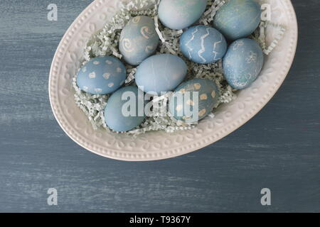 Les oeufs de Pâques peints de couleur, avec la teinture de chou rouge, dans un bol sur un tableau noir-bleu peint table de cuisine en bois vieilli. Banque D'Images