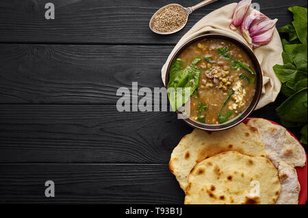 Mung Dhal, épinards, Chapati, d'ail et d'épices à table en bois noir. Moong Dal - la cuisine indienne, le curry. Plat épicé végétarien.top view Copy Space Banque D'Images