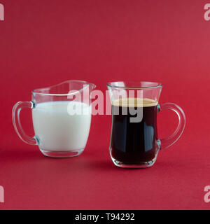 Tasse de café noir transparent et pot à lait, placé sur une surface rouge Banque D'Images