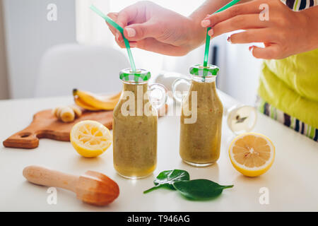 Bouteilles avec des épinards et banana smoothie d'ingrédients sur une table de cuisine. Femme met des pailles dans les boissons. Régime de detox en bonne santé Banque D'Images