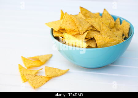 En forme de triangle jaune maïs croustillant nachos placés dans un bol bleu sur une table en bois blanc, certains d'entre eux jeter dehors. Banque D'Images