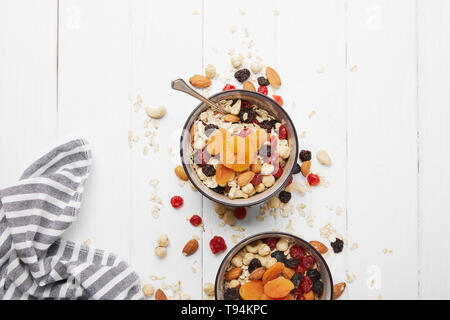 Vue de dessus de la pétanque avec du muesli, des abricots séchés et les fruits et les écrous pour le petit-déjeuner avec des ingrédients sur la table en bois blanc Banque D'Images