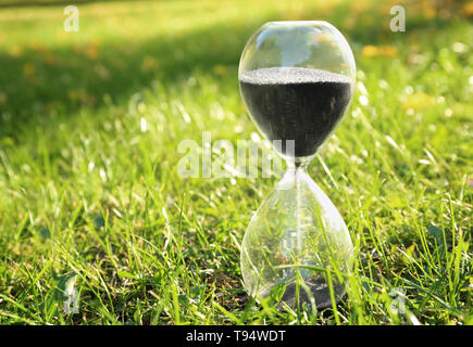 Sablier de cristal de sable noir sur l'herbe verte à l'extérieur Banque D'Images