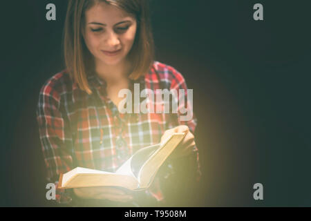 Jeune femme readin bible dans une pièce sombre Banque D'Images