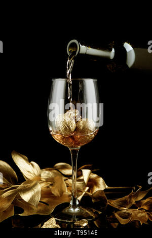 Coulée de vin rose de la bouteille en verre avec les noix d'or sur fond sombre Banque D'Images