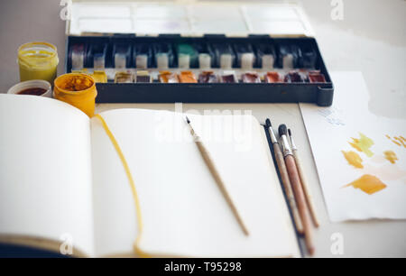 Le Bureau de l'artiste sur lequel sketchbook, pinceaux, Aquarelle et gouache et d'un morceau de papier sur lequel pour mélanger la peinture. Le bloc-notes de feuilles blanches Banque D'Images