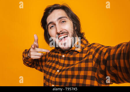 Portrait d'homme portant joyeuse allégresse chemise à carreaux et la prise de photo tout en selfies isolés sur fond jaune en studio Banque D'Images