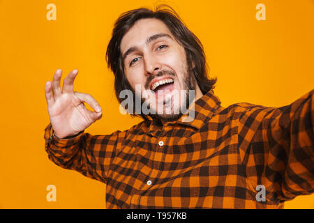 Portrait of caucasian man wearing plaid shirt réjouissance et de prendre tout en photo selfies isolés sur fond jaune en studio Banque D'Images