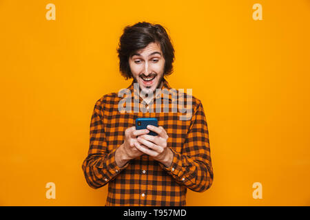 Photo de l'homme moustachu portant chemise à carreaux de rire et de l'utilisation du téléphone cellulaire isolés sur fond jaune en studio Banque D'Images