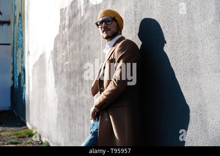 Beau Portrait d'homme barbu habillé dans des vêtements à la mode sur fond de mur gris contre rue Banque D'Images