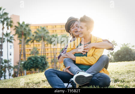 Heureux couple gay dans une date romantique hugging et rire ensemble assis sur l'herbe dans un parc - jeunes lesbiennes ayant un moment de tendresse outdoor Banque D'Images