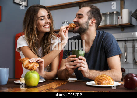Portrait d'homme et femme couple eating croissants pendant le petit-déjeuner dans la cuisine élégante Banque D'Images