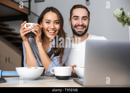 Heureux couple multiethnique le petit-déjeuner à la cuisine, looking at laptop computer Banque D'Images