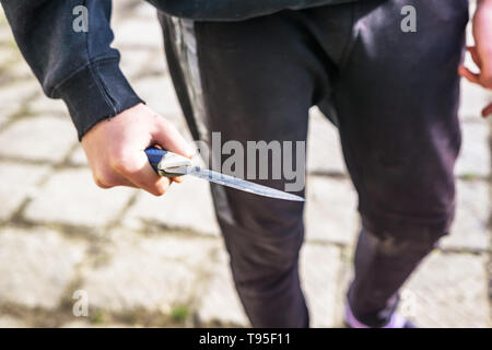 Close-up of a young man's hand avec un couteau, une grande lame. L'arrogance et la violence chez les jeunes. Peu de profondeur de foyer. Banque D'Images