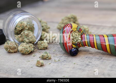 Tuyau en verre coloré avec de la Marijuana entouré par pot ouvert du Cannabis Sitting on Table Banque D'Images