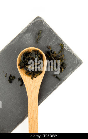 Petits morceaux de wakame séché (Undaria Pinnatifida), algues comestibles, ingrédient d'aliments différents dans la cuillère en bois sur pierre noire à découper isoler Banque D'Images