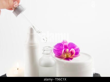 Femme part prendre de l'acide hyaluronique ou collagène liquide à la pipette à partir de la bouteille de verre, pots de crème sur l'arrière-plan, selective focus on compte-gouttes et liquides Banque D'Images