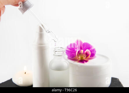 Femme part prendre de l'acide hyaluronique ou collagène liquide à la pipette à partir de la bouteille de verre, pots de crème sur l'arrière-plan, selective focus on compte-gouttes et liquides Banque D'Images